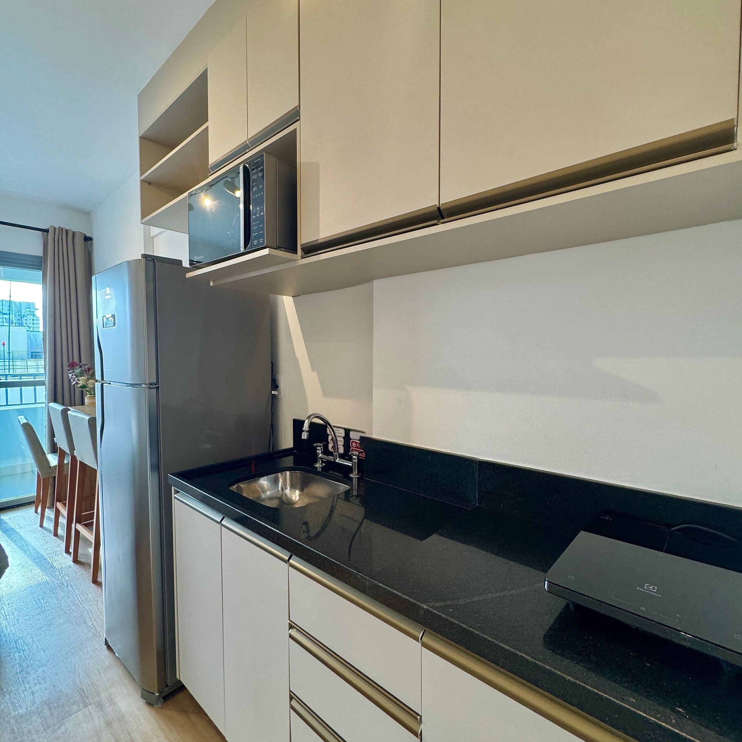 Una cocina moderna con un refrigerador de acero inoxidable, un microondas integrado y una encimera negra.