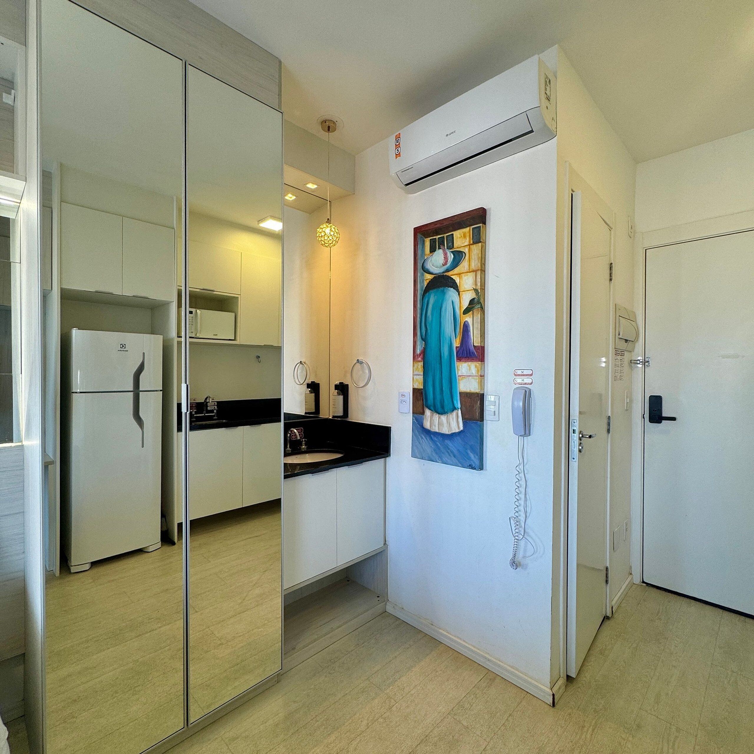 A compact kitchen with a refrigerator, a sink, and a painting on the wall.