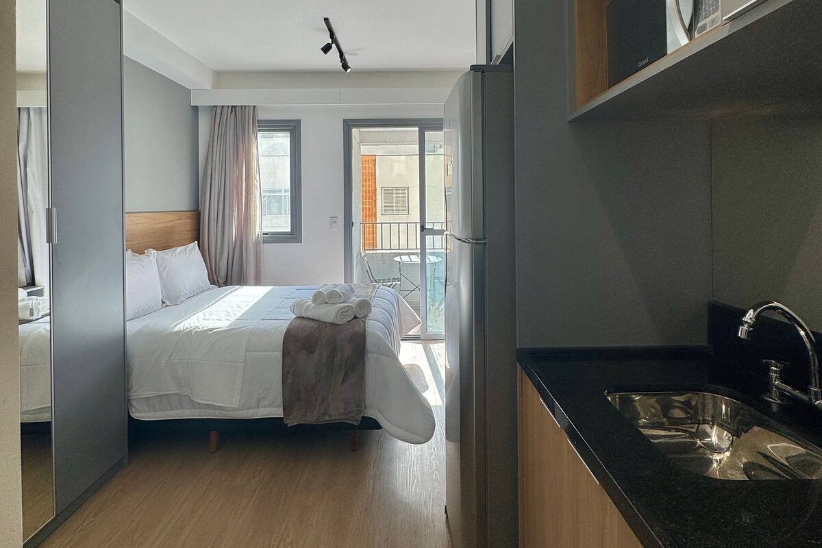 A modern hotel room with a bed, a bathroom, and a kitchen area.