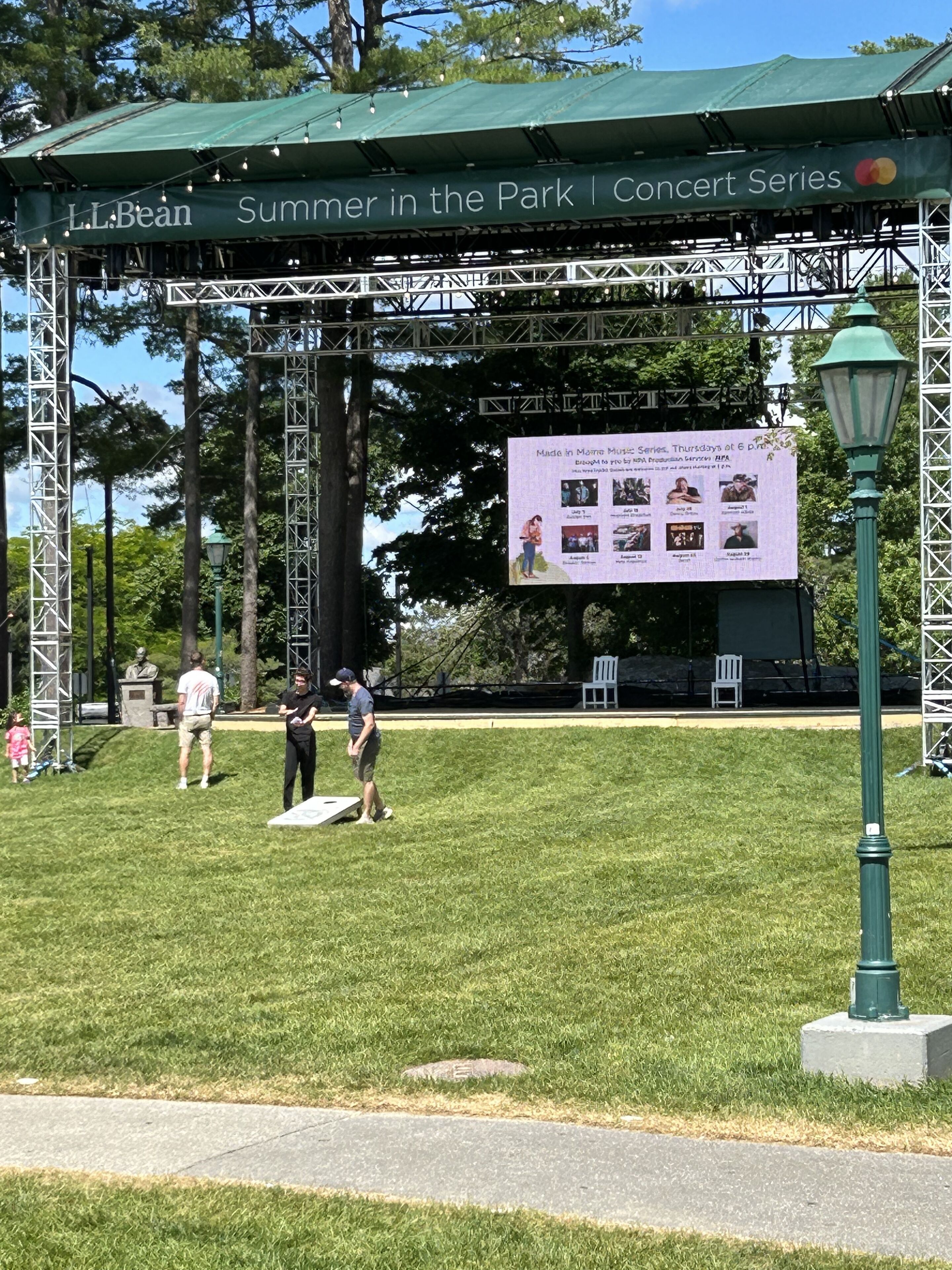 Eine Parkbühne mit einem grünen Baldachin, auf dem 'L.L.Bean Sommer im Park | Konzertreihe' steht, und ein Plakat, das die Made in Maine Musikreihe bewirbt.
