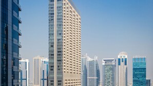 A high-rise building with a modern design, a marina with several boats docked, and a clear blue sky. - Handsome 1BR in Bay Central Tower (Dubai)