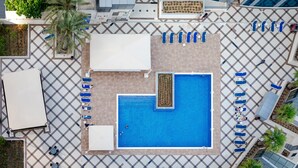 An aerial view of a hotel pool area with a checkered floor pattern, a central swimming pool, and multiple lounge chairs arranged around the pool. - Handsome 1BR in Bay Central Tower (Dubai)