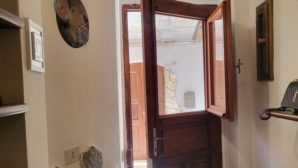 A hallway with a wooden door, a stone wall, and a tiled floor. - La Piccola Casetta nel Centro Storico (Iglesias)