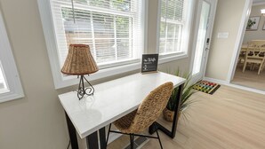 Un comedor con una mesa blanca, sillas de mimbre y un cartel que indica la contraseña de WiFi.