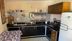 Eine kompakte Küche mit Kühlschrank, Herd, Mikrowelle und einer kleinen Essecke mit einem blumigen Tischlaken.