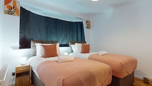 A hotel room with two beds, a nightstand, a lamp, and a window with curtains. - Dagenham - 4 Beds - Sleeps 8 - Wifi (Dagenham)