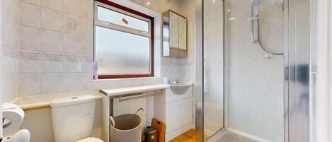 A modern bathroom with a glass shower enclosure, a toilet, a sink, and a window.