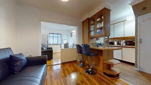 A modern living room with a sofa, a dining area with chairs, and a kitchen with wooden cabinets. - Dagenham - 4 Beds - Sleeps 8 - Wifi (Dagenham)
