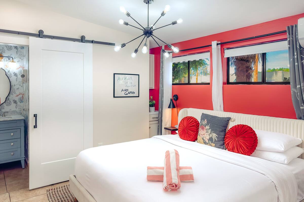 A bedroom with a bed, a white door, a red wall, and a ceiling light fixture.