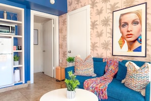 A living room with a blue sofa, colorful pillows, a white coffee table, and a framed picture on the wall. - The Muse Hotel (Adults only 15+) (Palm Springs)