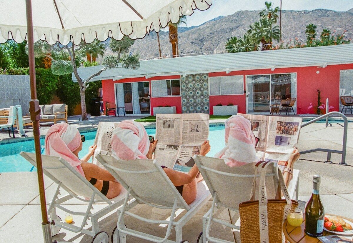 A poolside area with lounge chairs, a table with a bottle and glass, and a building with large windows in the background.