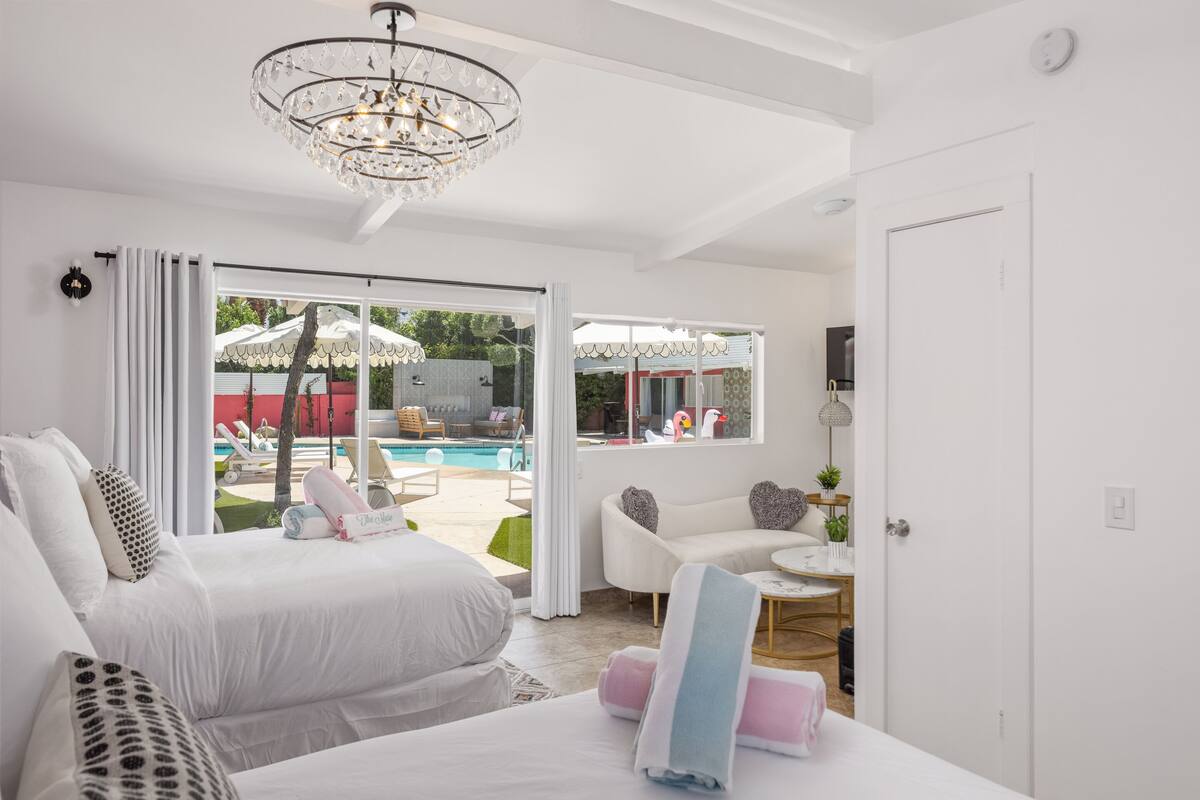 A modern hotel room with a large bed, a sitting area with a white sofa, and a view of an outdoor pool area.
