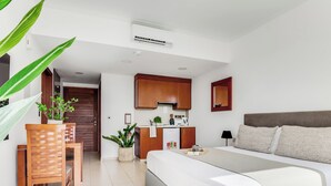 A modern hotel room with a bed, a small kitchenette, a wooden dining table, and a potted plant. - Sanders Seaview Paphos (Chlorakas)