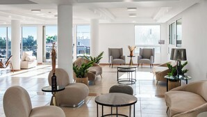 A modern hotel lobby with beige sofas, round tables, and potted plants. - Sanders Seaview Paphos (Chlorakas)