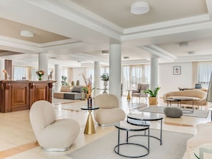 A spacious lobby with a reception desk, seating area with sofas and armchairs, a coffee table, and a dining table. - Sanders Seaview Paphos (Chlorakas)