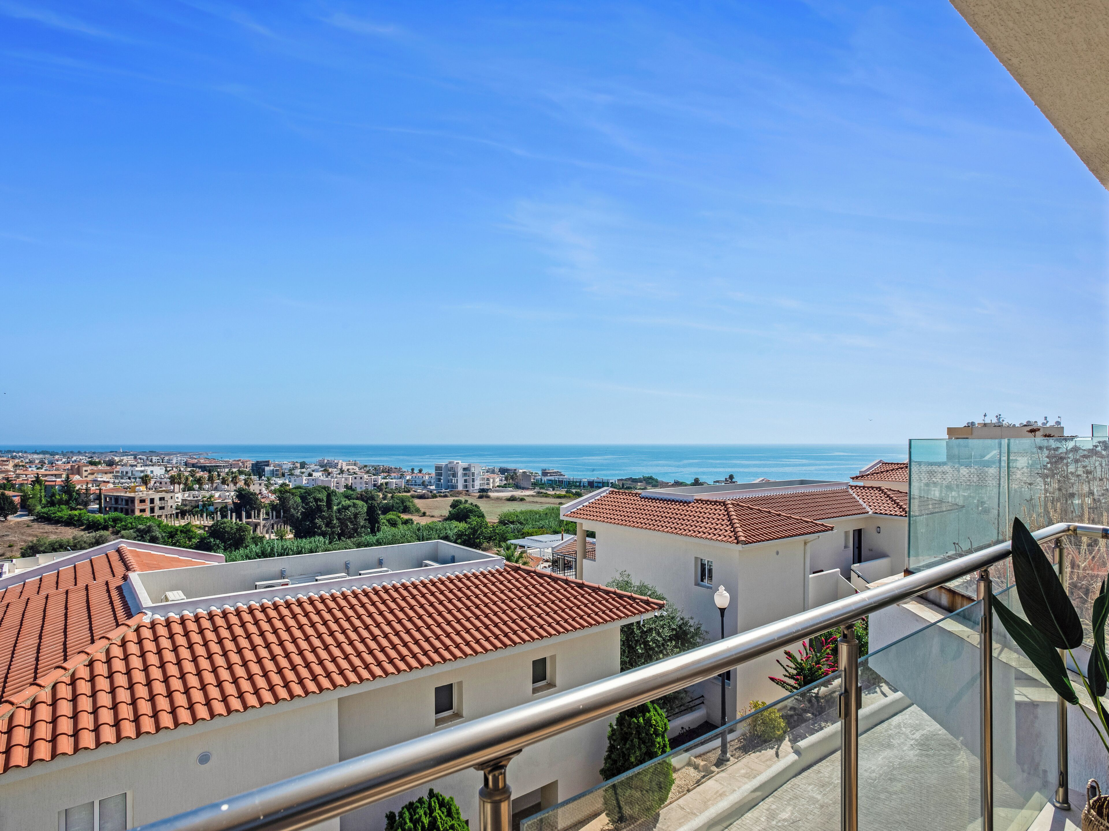 Un quartier résidentiel offrant une vue dégagée sur la mer, avec des bâtiments aux toits de tuiles et un balcon doté d’une balustrade en verre.