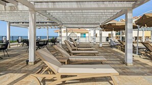 A covered outdoor seating area with lounge chairs and tables, a pergola overhead, and a view of the sea in the background. - Sanders Seaview Paphos (Chlorakas)