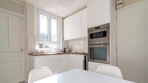 A modern kitchen with white cabinetry, a double oven, and a dining area with a white table and chairs. - MM Suites Cathedrale (Reims)