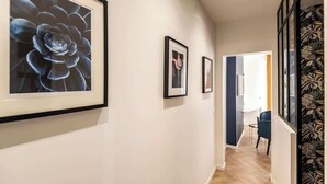 Un pasillo con obras enmarcadas en las paredes, suelo de madera y una silla azul al fondo.