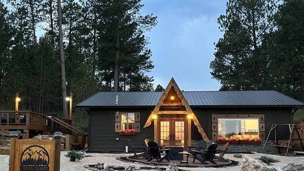 Eine Lodge mit Holzfassade, einer Veranda mit Sitzgelegenheiten und einem Schild, das es als Cedar Chalet kennzeichnet.