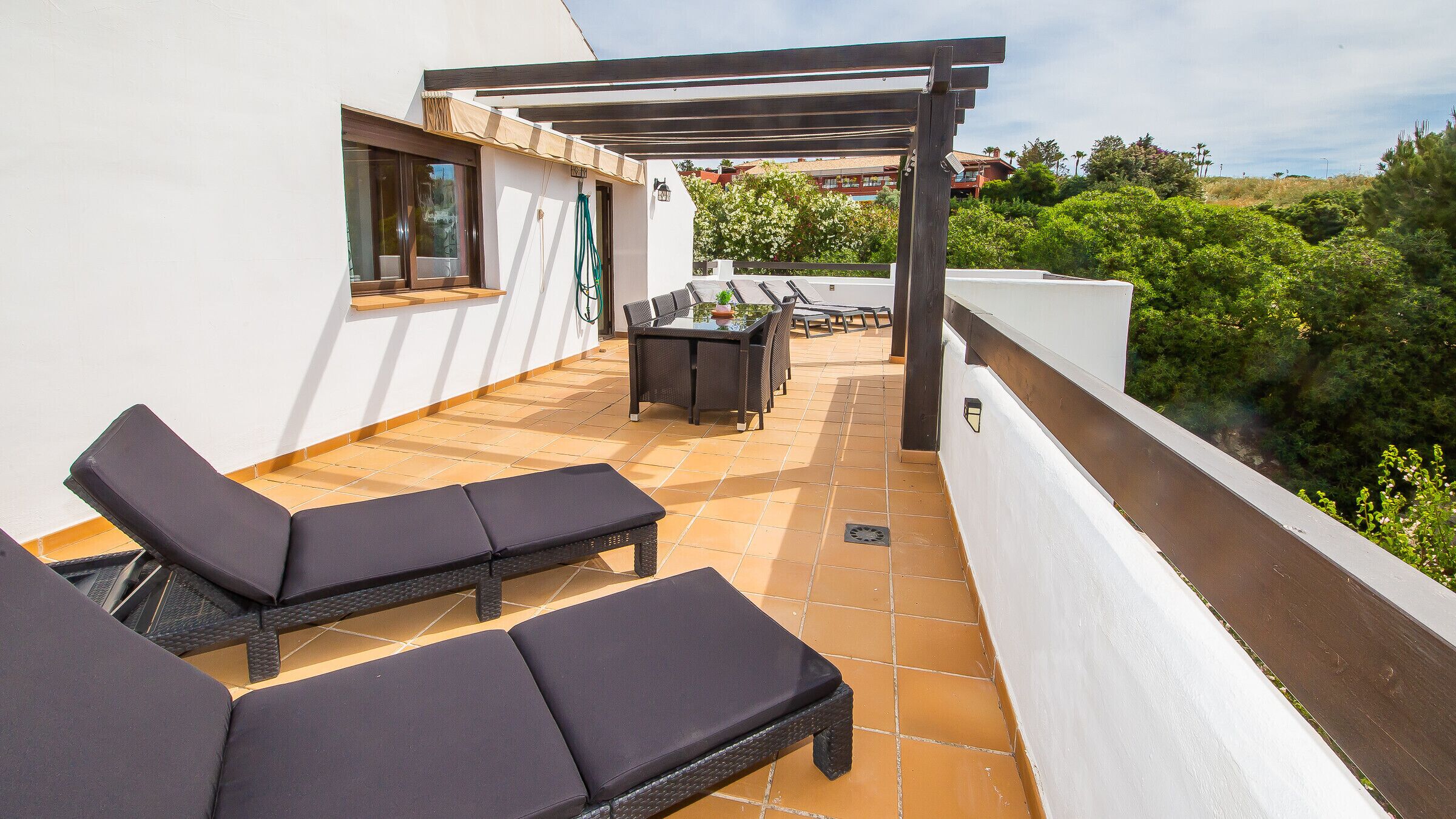Eine Dachterrasse mit zwei Liegestühlen, einem Tisch und Stühlen sowie einer Pergola.