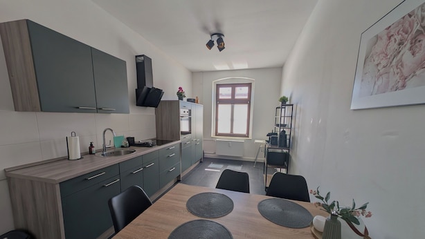 Una cucina compatta con zona pranzo, forno integrato e finestra con persiane.