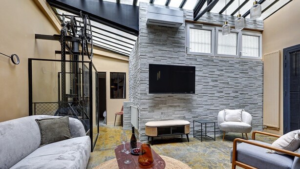 A modern living room with a stone wall, a mounted TV, and a seating area with a sofa and chairs. - 399 Suite Loft XV - Superb Apartment in Paris (Paris 15 Vaugirard)