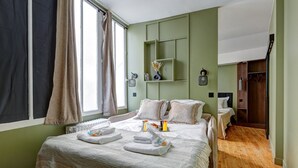 A hotel room with a large bed, a smaller bed, a wooden floor, a window with curtains, and a green wall. - 399 Suite Loft XV - Superb Apartment in Paris (Paris 15 Vaugirard)