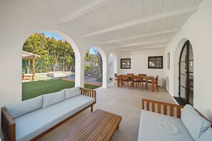 A covered outdoor patio with a sofa, wooden table, and dining set. - Bella Villa (Los Angeles)