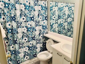 A bathroom with a mosaic-patterned shower curtain, a toilet, and a sink with a mirror.
