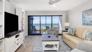 A living room with a television, a sofa, a coffee table, and a view of the ocean through large windows. - All New! Gulf Front! High End! Pelicans Roost 303 on Sanibel Island (Sanibel)