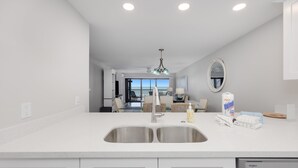 A modern kitchen with a double sink, a dishwasher, and a view to the living area. - All New! Gulf Front! High End! Pelicans Roost 303 on Sanibel Island (Sanibel)