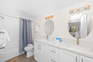 A modern bathroom with a white sink, vanity, and toilet. There are two mirrors, one oval and one rectangular, and a shower curtain.
