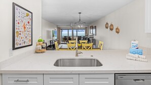 A modern kitchen with a large island, stainless steel sink, and a view to the dining area.