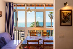 A room with a view of the sea, a dining table with chairs, a sofa, and a hanging light fixture.