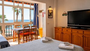 A hotel room with a bed, a television, a dining table with chairs, and a view of the sea.