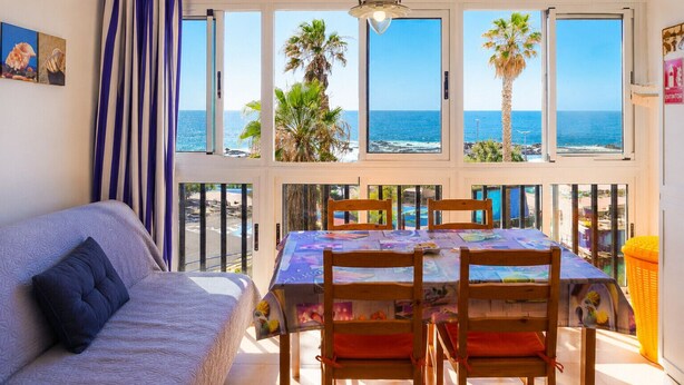A room with a balcony, a table with chairs, a sofa, and a view of the sea.