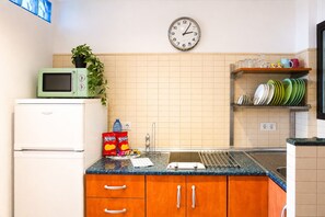 A kitchen with a microwave, a clock, a sink, and a shelf with plates.