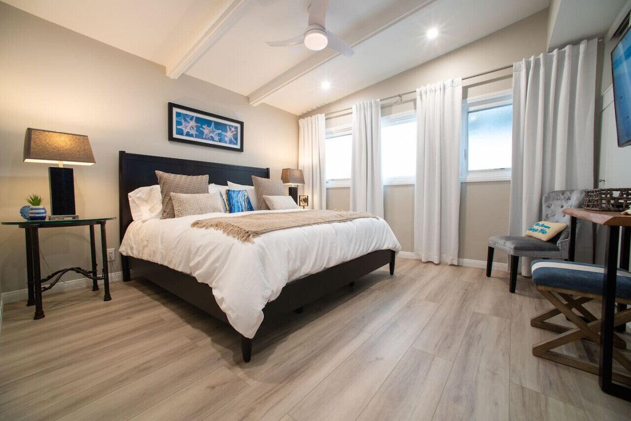 Un dormitorio con cama, mesitas de noche, una silla, ventilador de techo y ventana con cortinas.