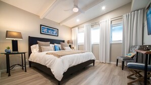 Une chambre à coucher comprenant un lit, des tables de chevet, une chaise, un ventilateur de plafond et une fenêtre avec des rideaux.
