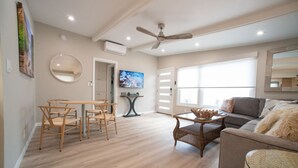 Un salon comprenant un canapé, une table à manger avec des chaises, un ventilateur de plafond et un téléviseur fixé au mur.