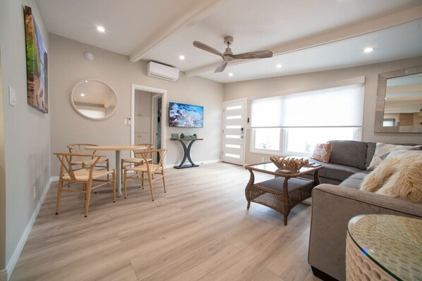 A living room with a sofa, a dining table with chairs, a ceiling fan, and a TV on the wall.
