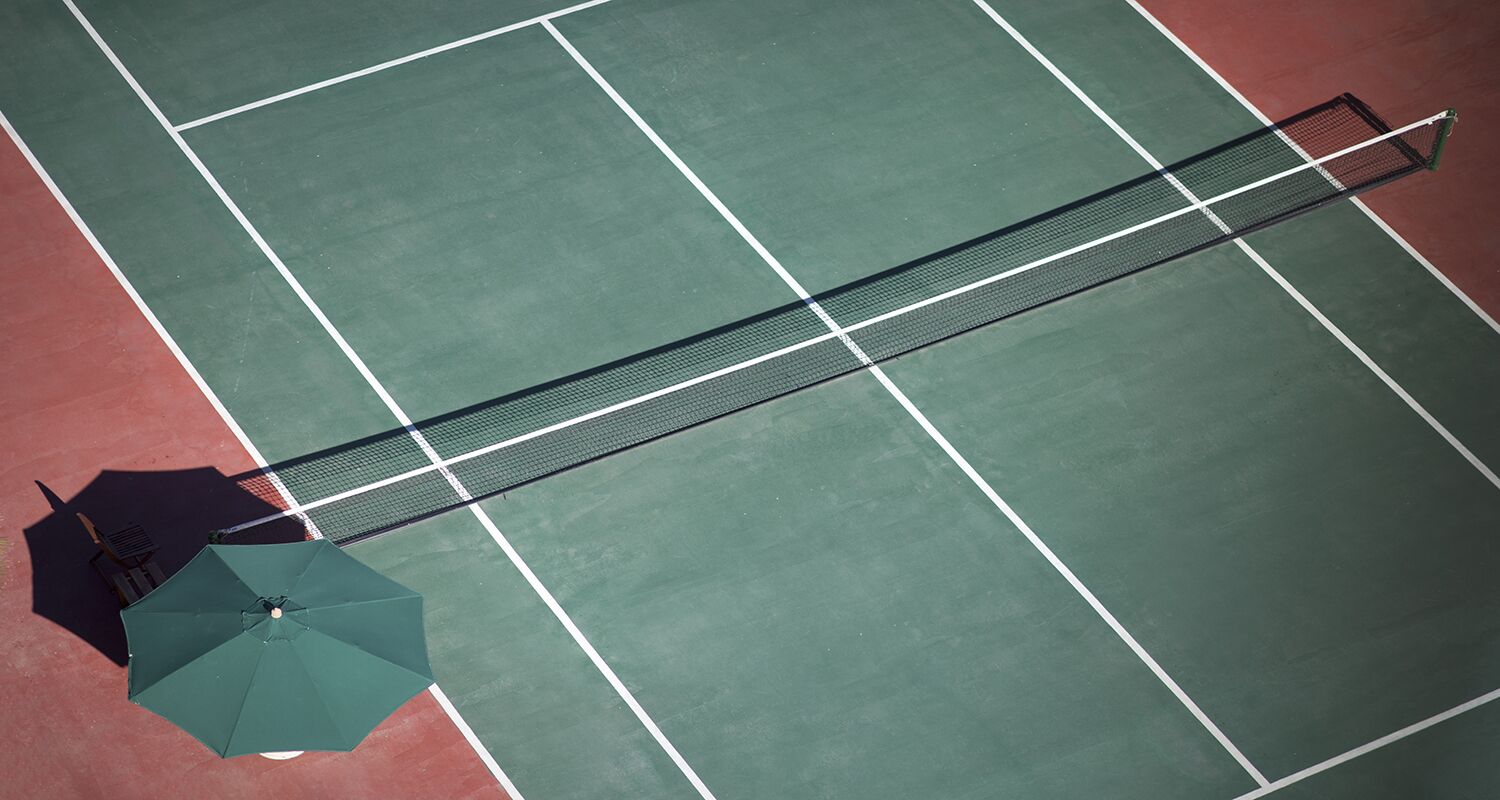 Una cancha de tenis con una red, un paraguas verde y una zona roja.