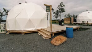 A geodesic dome structure with a wooden deck and a signboard. - Beachcomber Dome Accommodations (Monks Head)