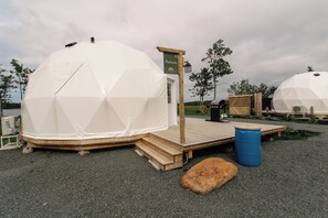 A geodesic dome structure with a wooden deck and a signboard. - Beachcomber Dome Accommodations (Monks Head)