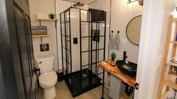 A compact bathroom with a toilet, a glass-enclosed shower, a sink with a black basin, and a mirror on the wall. - Beachcomber Dome Accommodations (Monks Head)