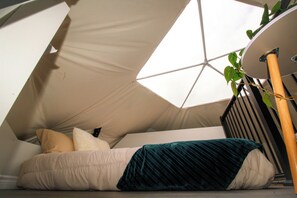 Une pièce triangulaire, chaleureuse et accueillante, avec un lit, des oreillers et une plante.