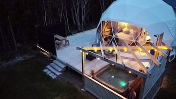 Uma tenda em forma de cúpula com deck de madeira, hidromassagem e luzes de corda.