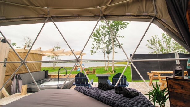 A tented accommodation with a view of a lake, a hot tub, and outdoor seating.