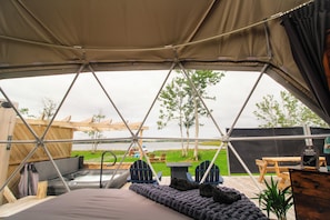 A tented accommodation with a view of a lake, a hot tub, and outdoor seating.